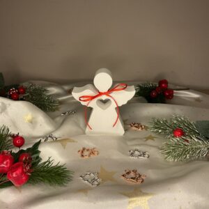 Λευκό πορσελάνινο διακοσμητικό σε σχήμα αγγέλου με κοψίματα καρδιάς και κόκκινη κορδέλα.