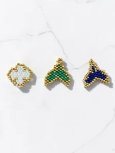 Charms Μικρο-Θαύματα φτιαγμένα με τεχνική peyote-stitch σε σχήμα σταυρού και ουράς με χρυσές λεπτομέρειες.