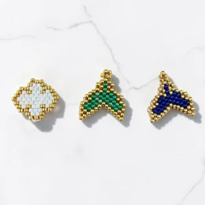 Charms Μικρο-Θαύματα φτιαγμένα με τεχνική peyote-stitch σε σχήμα σταυρού και ουράς με χρυσές λεπτομέρειες.