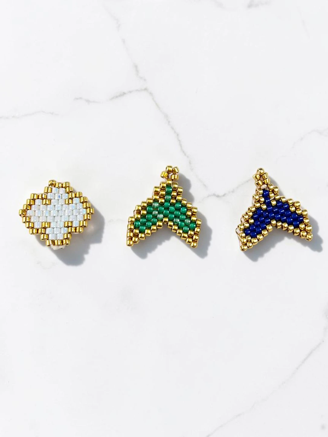 Charms Μικρο-Θαύματα φτιαγμένα με τεχνική peyote-stitch σε σχήμα σταυρού και ουράς με χρυσές λεπτομέρειες.